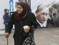 Пожилая женщина на фоне плаката с Владимиром Путиным в Санкт-Петербурге Пожилая женщина на фоне плаката с Владимиром Путиным в Санкт-Петербурге