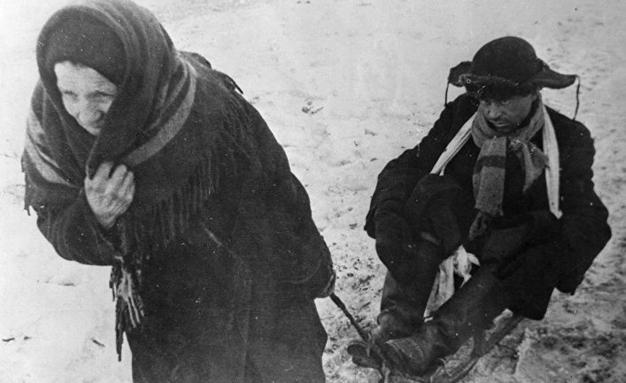 Жители блокадного Ленинграда: женщина везет ослабевшего от голода мужа на санках