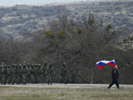 Местный житель с флагом и российские военные рядом с украинской военной базой в деревне Перевальное под Симферополем Местный житель с флагом и российские военные рядом с украинской военной базой в деревне Перевальное под Симферополем, 2 марта 2014 года
