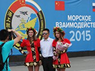 Участник китайской делегации фотографируется с русскими девушками на фоне баннера совместных учений "Морское взаимодействие - 2015"