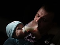 Отец кормит ребенка из из бутылочки на фестивале BabyFest в Сокольниках Отец кормит ребенка из из бутылочки на фестивале BabyFest в Сокольниках