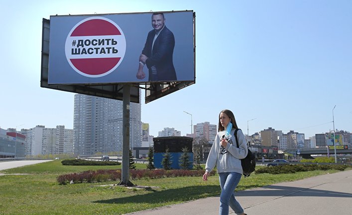 Девушка у рекламного щита, установленного в Киеве в связи с коронавирусом. Надпись: «Хватит шастать»
